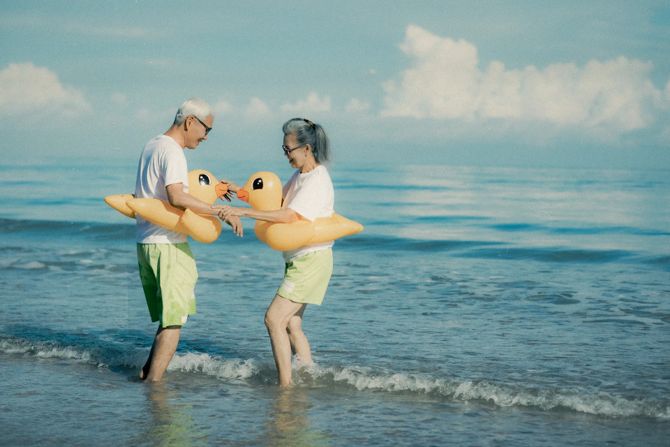 An older asian couple with bright yellow duck floaties on playing in the ocean