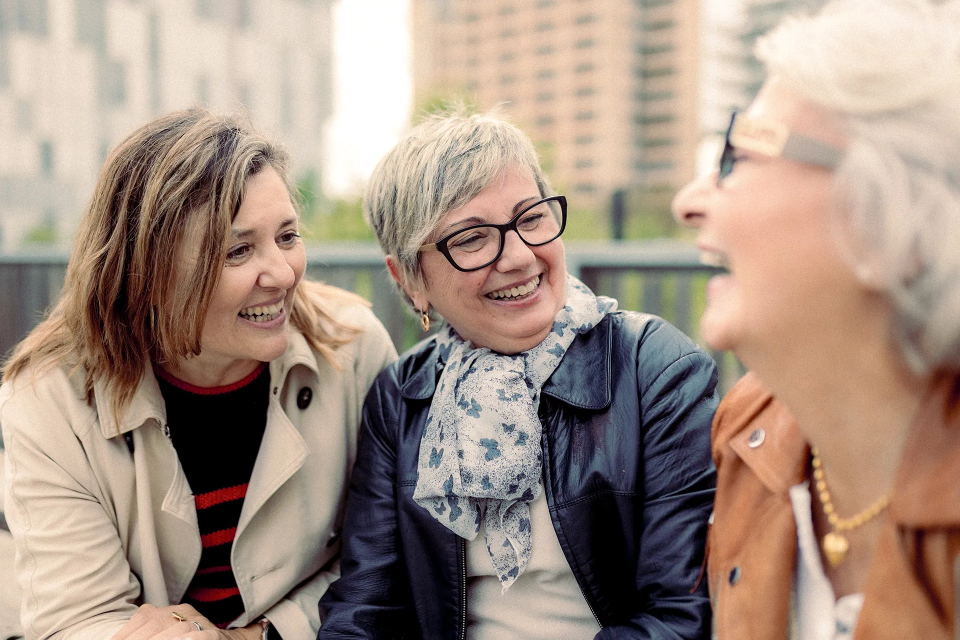Three women sitting closely together with smiles on their faces on a sunny day