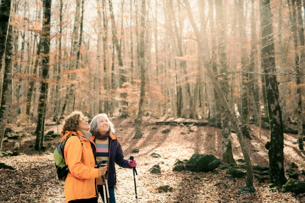 two women hiking in the woods looking up smiling 