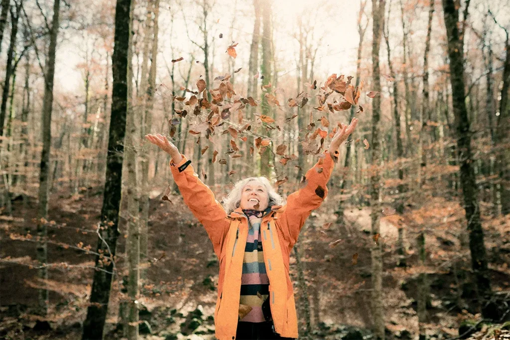 older caucasian woman hilking throwing leaves into the air 