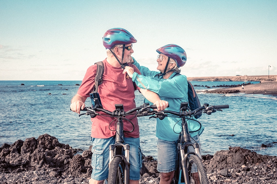 couple biking by the sea, woman helping man with helmet